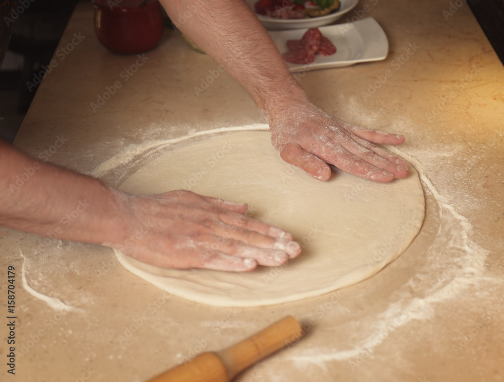 Cook preparing dough for pizza on kitchen table