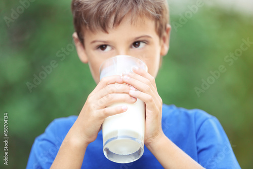 Cute boy in blue shirt drinking milk on blurred background