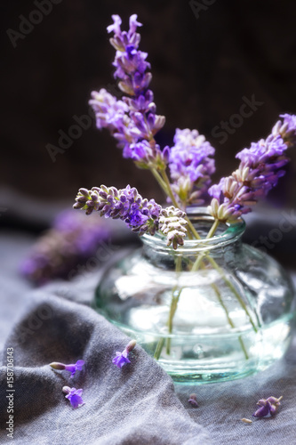 Small bunch of lavender flowers in a glass vase against dark background. Shallow depth of field