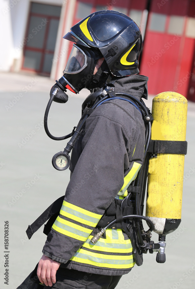 Fototapeta premium Firefighter with large yellow oxygen cylinder and protective hel