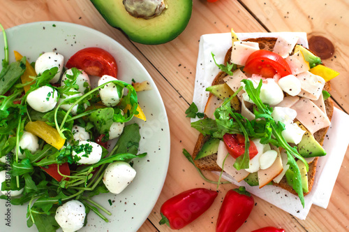 Salad with mozzarella, arugula and sandwich with avocado, ham. Wooden background. Close-up. Top view
