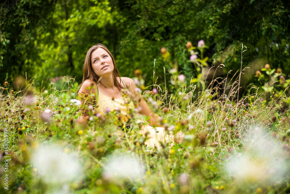 Beautiful woman enjoys nature in summer bloom. Lonely girl has a beautiful face. The woman sits in the meadow. Blurry background. Beautiful woman enjoys nature in summer bloom. Lonely girl has a beautiful face. The woman sits in the meadow. Blurry background.