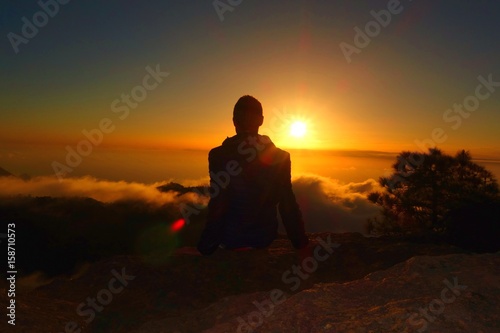 Mountain landscape at sunset with a silhouette of a relaxed teenage boy