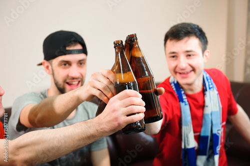 Young men drink beer, eat chips and root for football © nagaets