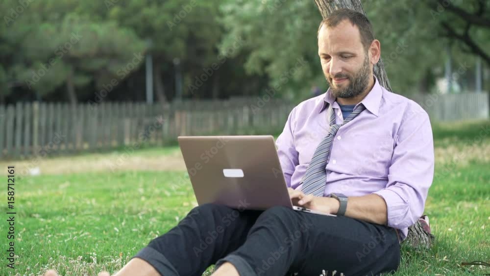 Young businessman working on laptop sitting on grass in park
Young businessman working on laptop sitting on grass in park