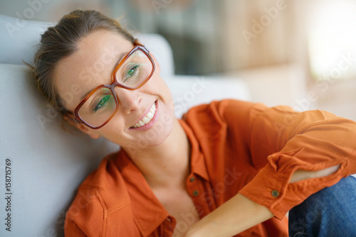 Cheerful girl with trendy eyeglasses sitting on floor at home