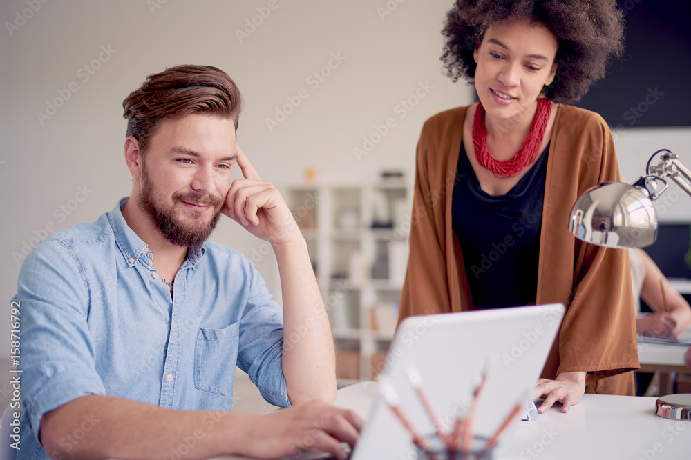 Businessman sitting and using laptop while his colleague standing and helping him Businessman sitting and using laptop while his colleague standing and helping him