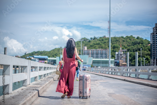 Selective focus Back of young business girl passenger walking down the walkway with a suitcase at the port. © Suntipong
