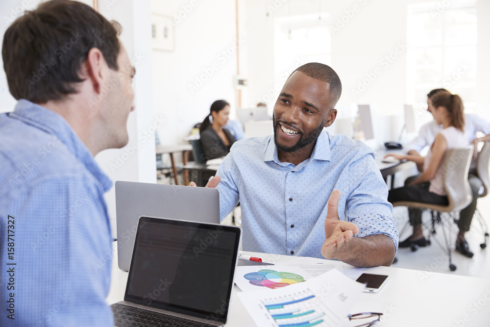 Two men discussing business in a busy office Two men discussing business in a busy office