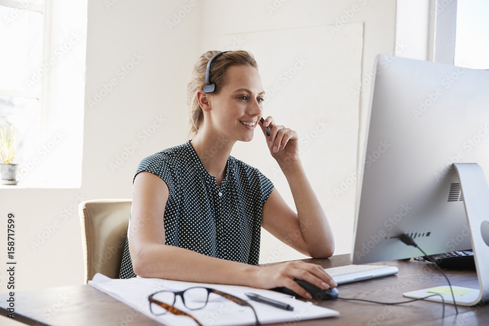 Smiling white woman at computer in an office wearing headset Smiling white woman at computer in an office wearing headset