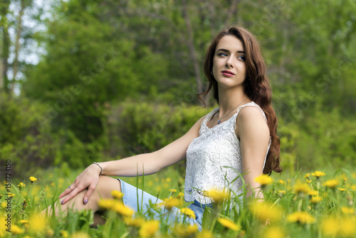 Girl with long hair sitting on the lawn with blooming dandelions