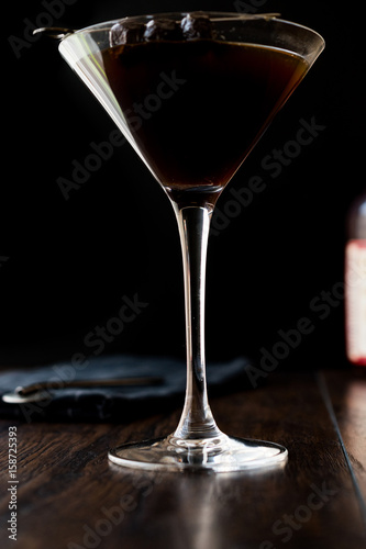 Black Manhattan Cocktail with olives on dark wooden surface.