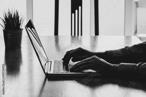 Man hands typing on a laptop in a workplace. Business black and white.