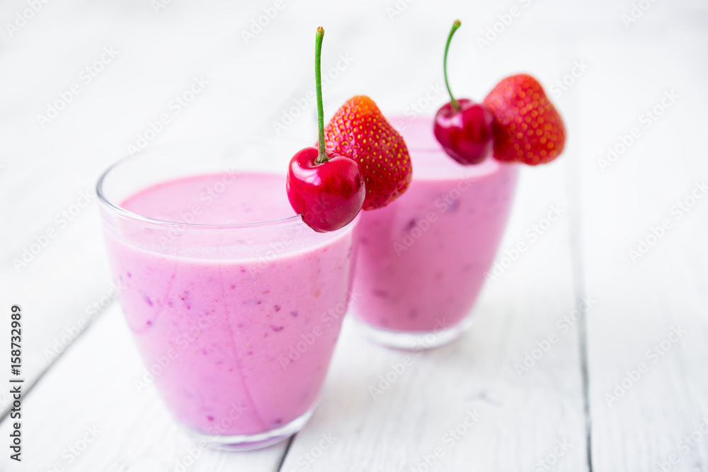Cherry and strawberry milkshake and tasty berries on white wooden table. Cherry and strawberry milkshake and tasty berries on white wooden table.