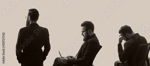 Three various silhouettes of a bearded man in a business suit with glasses on toned background. Black and white image.