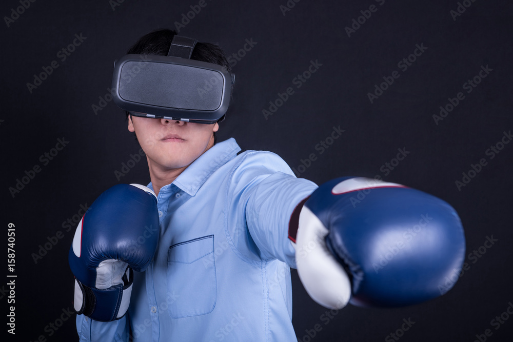 young asian man wearing virtual reality goggles with black background studio in fighting pose. Smartphone using with VR headset. young asian man wearing virtual reality goggles with black background studio in fighting pose. Smartphone using with VR headset.
