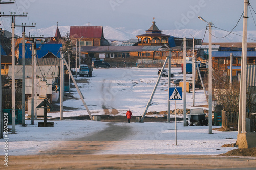a small town or village of khuzhir on Olkhon. quite empty street but full of snow. Electricity poles lie on the sides of the street and crossing sign on the left. the crossing sign in blue.  photo