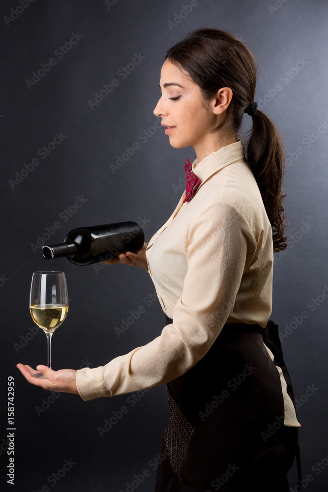 Cameriera di profilo con camicia beige e papillon rosso su sfondo scuro,  versa il vino in un calice di cristallo Stock Photo | Adobe Stock