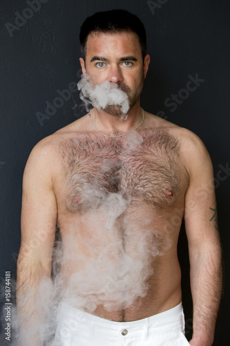 man with naked chest blowing out cigarette smoke
