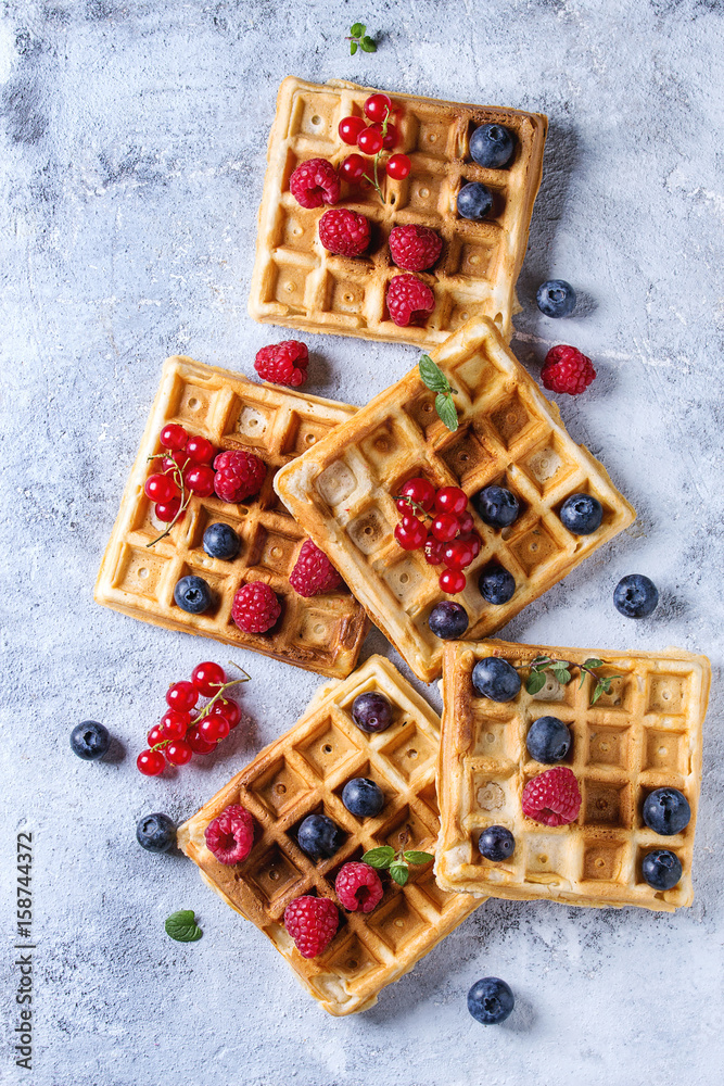 Homemade square belgian waffles with fresh ripe berries blueberry, raspberry, red currant over gray texture background. Top view with space