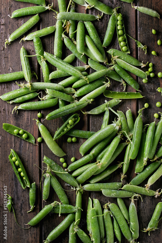 Young organic green pea pods and peas over old dark wooden planks background. Top view with space. Harvest, healthy eating.