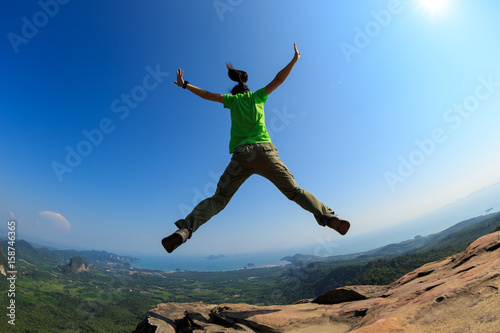 successful woman jumping on rocky mountain peak