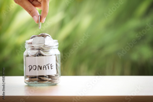 Vászonkép Hand putting Coins in glass jar for giving and donation concept