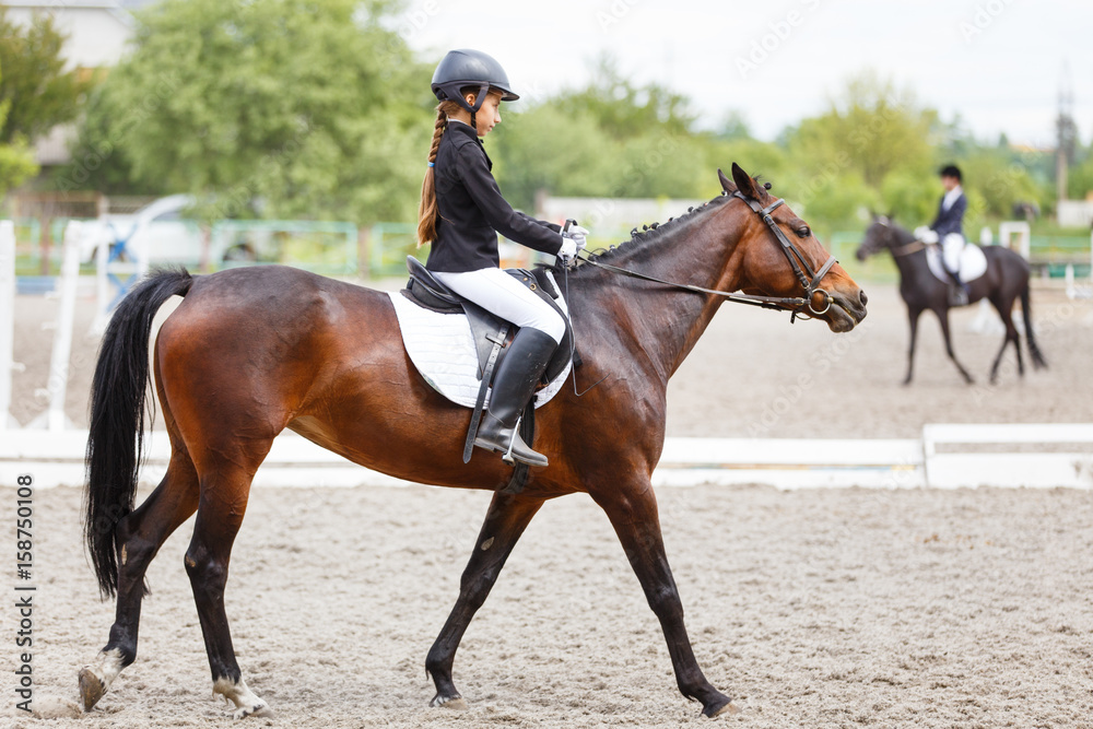 Young teenage girl in helmet riding horse on dressage equestrian competition Young teenage girl in helmet riding horse on dressage equestrian competition