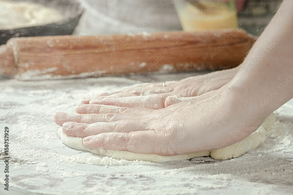 female hands in flour kneading dough on table