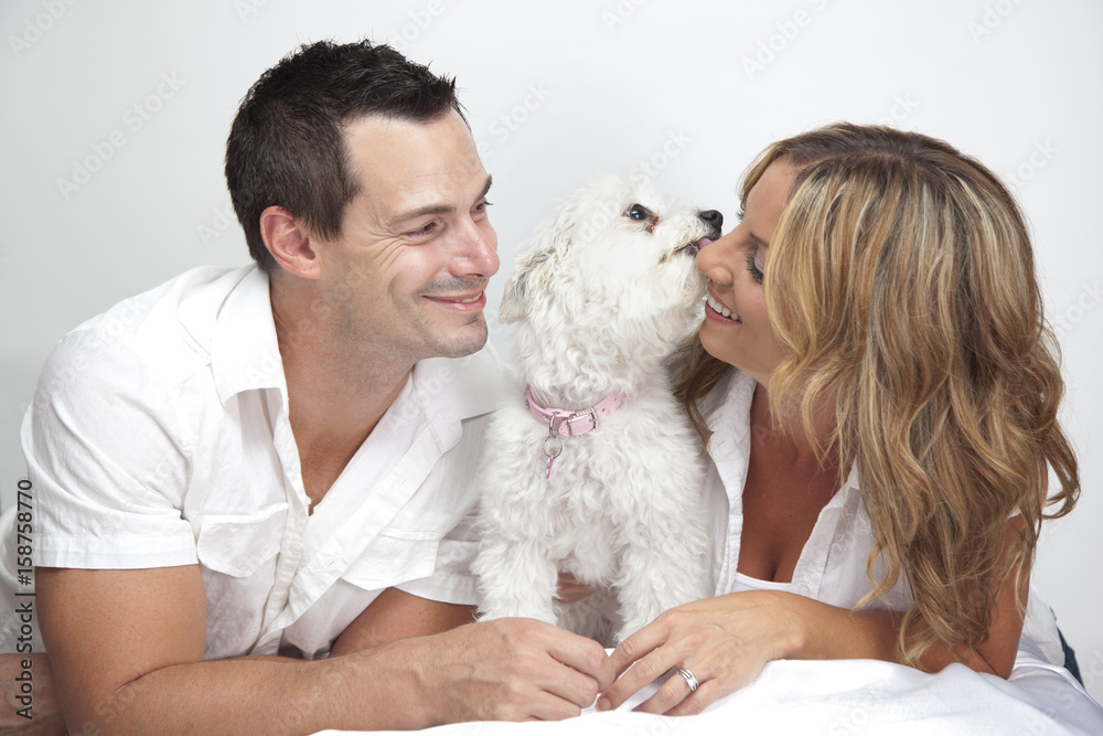 Obraz premium Happy couple with young pet dog, puppy kissing woman.