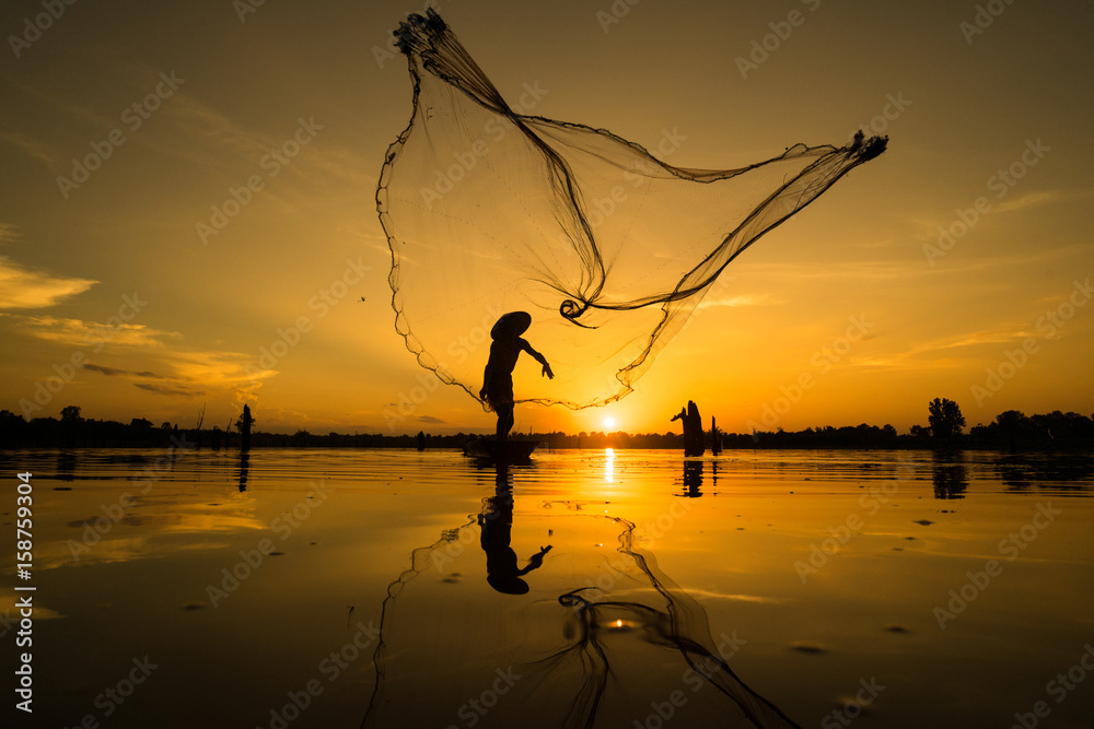 Silhouette of Fisherman catching fish in lake by using fishing net at  beautiful sunset time. Stock Photo