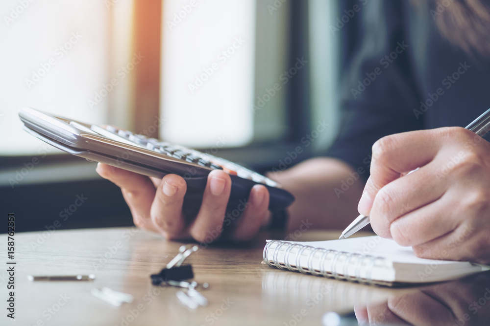 Fototapeta premium Closeup image of a business woman working , using calculator and writing on notebook in office