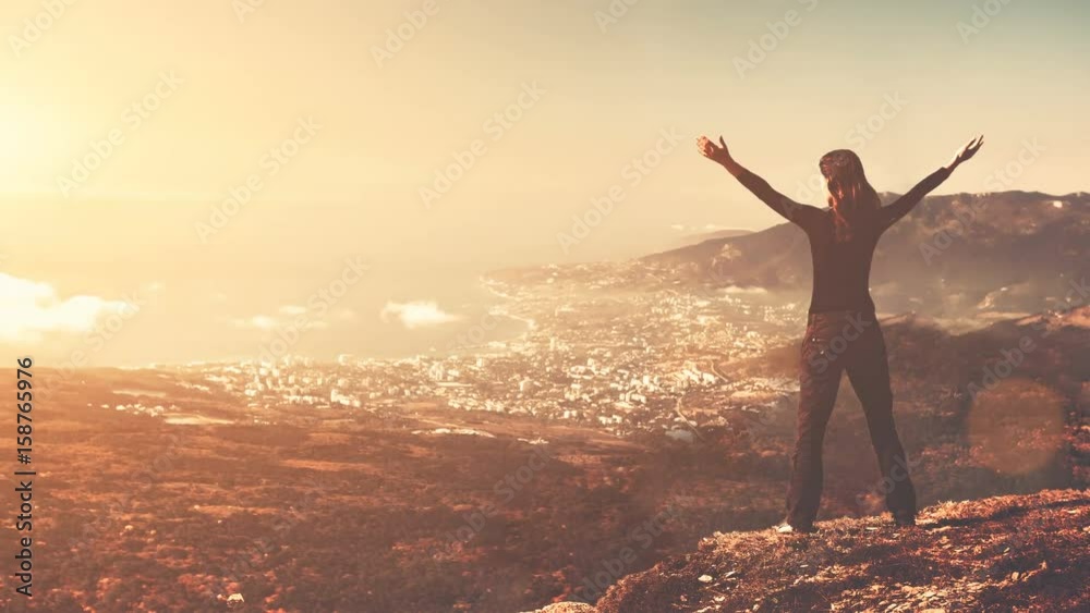 Young woman silhouette with arms up standing on the mountain peak ...