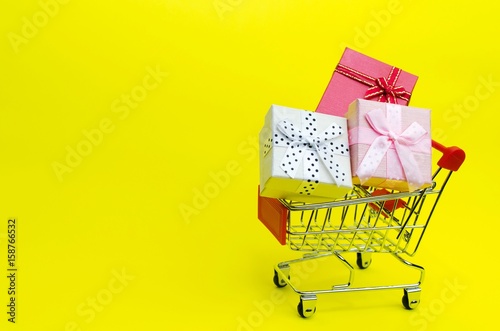 mini colorful gifts box in mini supermarket shopping cart on yellow background, holiday sale concept, selective focus, copy space
