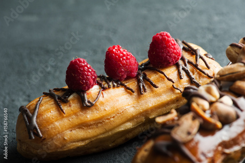 Fotografie Eclairs with peanuts, chocolate icing and raspberries