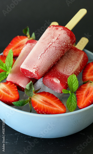 Homemade strawberry ice cream popsicles on dark background.