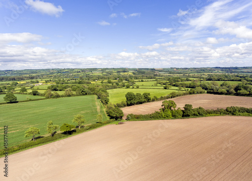 Aerial view of farm fields with ploughed brown fields, green pastures, meadows, in an English, summer countryside .