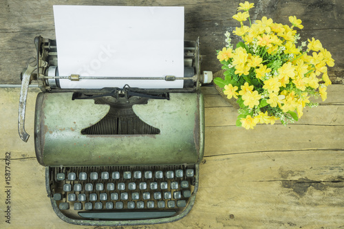  top view of Old typewriter with blank paper,retro typewriter on table ,Retro typewriter placed on wooden planks, typewriter and a blank sheet of paper and flower pot ,vintage tone,selective focus.