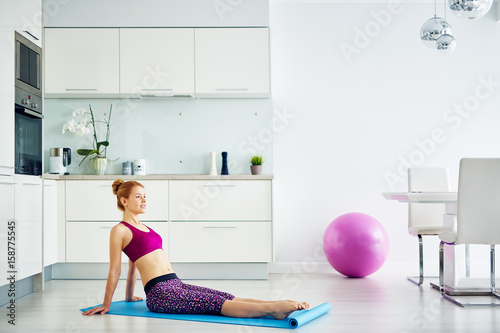 Portrait of fit red haired woman doing yoga exercises at home on floor