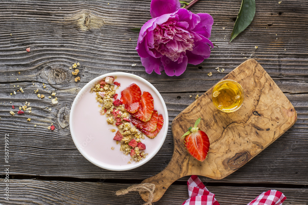 Strawberry yogurt with granola, sliced berries on a wooden background in a white ceramic bowl. Top view