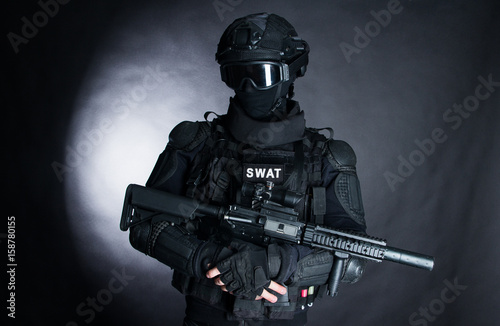 Member of the SWAT squad with an assault rifle in a black uniform on dark background. Special weapons and tactics. Special Forces.