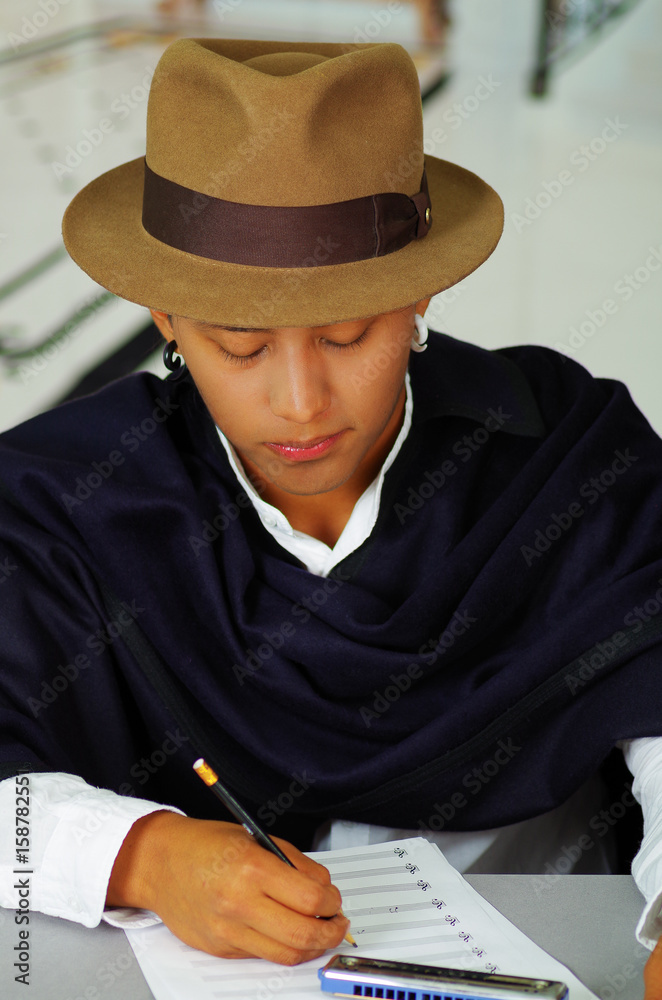Indigenous young man writing notes to music with harmonica, concept of composition Indigenous young man writing notes to music with harmonica, concept of composition