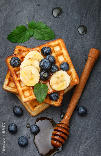 Traditional Belgian waffles with blueberries, banana and honey on a black slate plate. Gourmet Breakfast. Selective focus