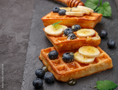 Traditional Belgian waffles with blueberries, banana and honey on a black slate plate. Gourmet Breakfast. Selective focus