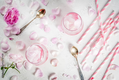 Summer refreshing desserts. Vegan diet food. Ice cream frozen rose, froze, with rose petals and rose wine. White concrete table, with spoons, striped straws, petals and flowers. Copy space top view