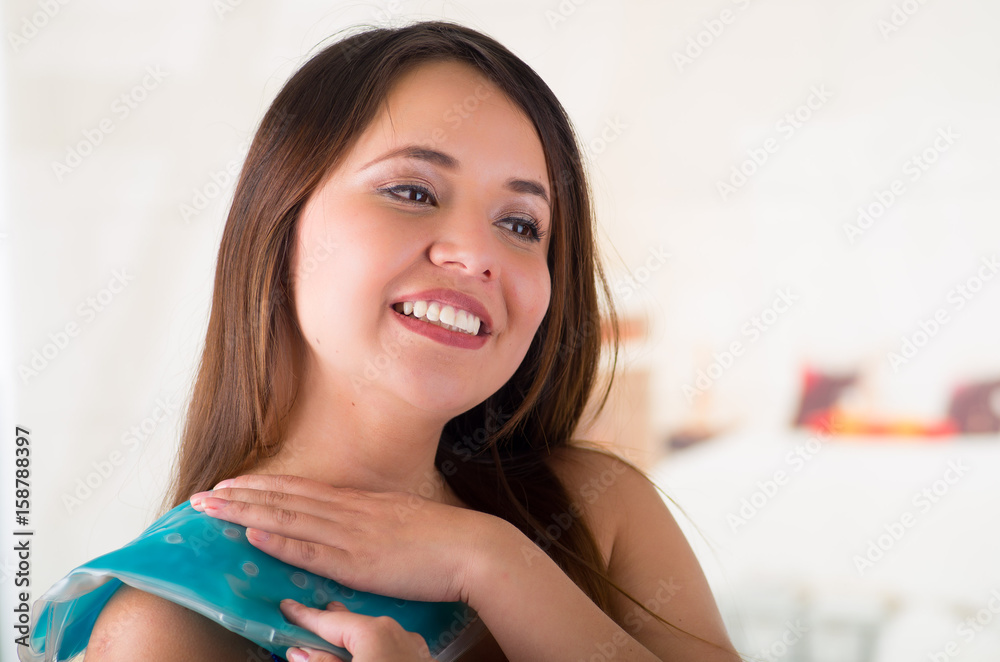Close up of a beautiful smiling woman holding ice gel pack on her shoulder, medical concept, in office background