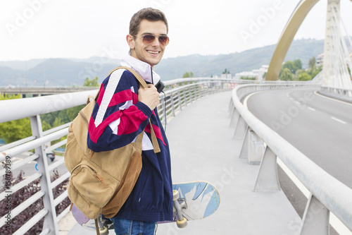 modern young man with the backpack and walking through the city skateboard