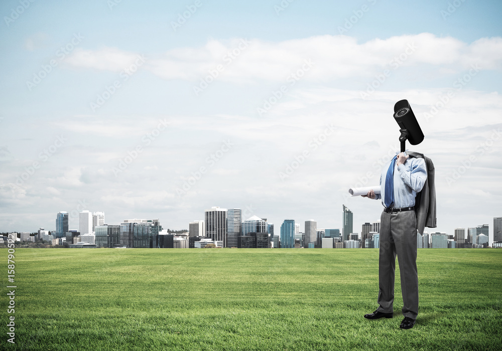 Camera headed man standing on green grass against modern citysca Camera headed man standing on green grass against modern citysca