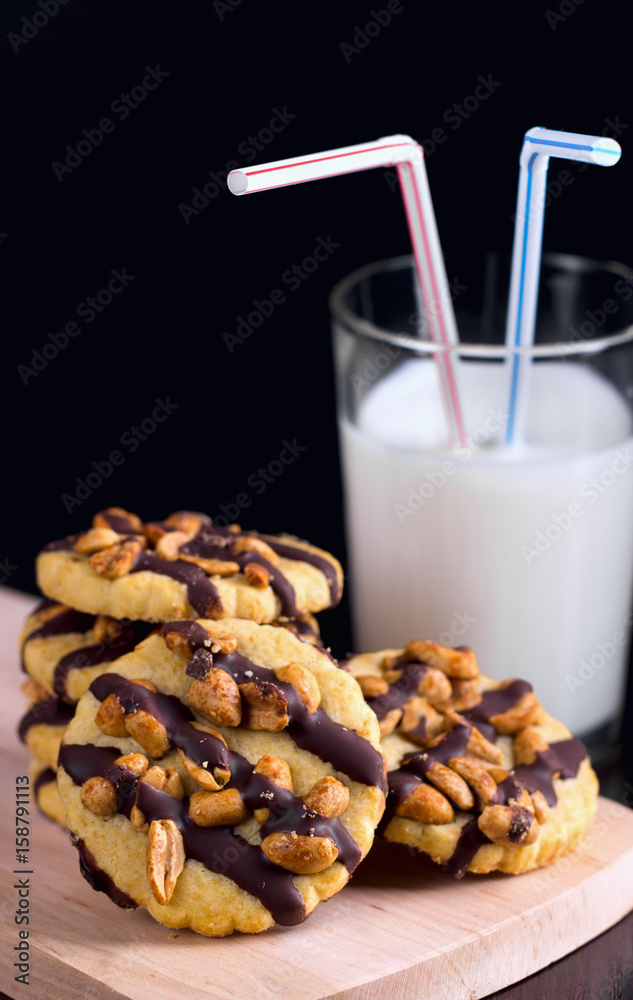Cookies with peanuts covered with chocolate icing, and a glass of milk on a dark wooden background. Cookies with peanuts covered with chocolate icing, and a glass of milk on a dark wooden background.