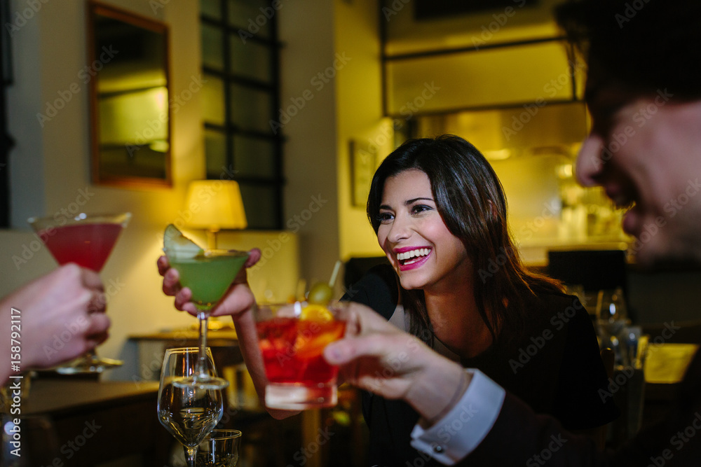 beautiful young woman toasting with friends at cocktail bar